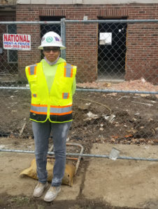 Della stands in her neon yellow vest and hard hat at the construction site.